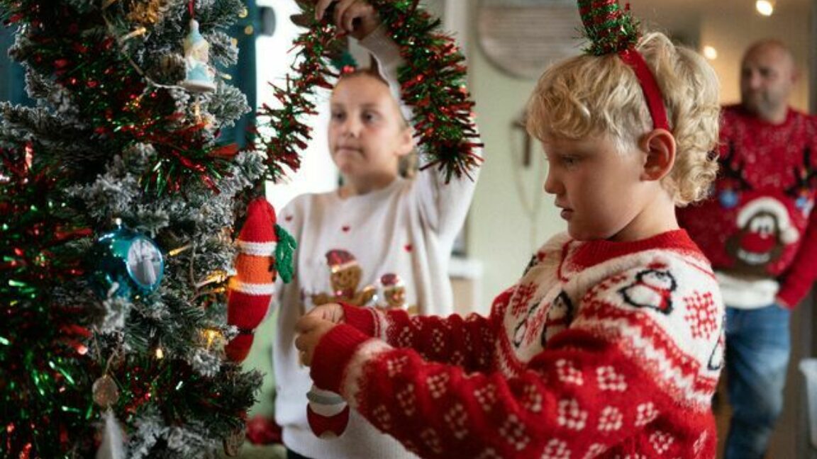 Two children wearing Christmas jumpers putting up Christmas decorations in their home