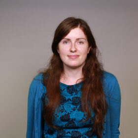 Claire Wong, Digital Content Producer and Copy Specialist. A white female with long brown hair and a blue, long sleeved top, smiling
