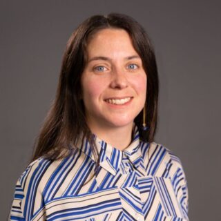 CAP employee, Lydia, with dark brown hair, wearing a blue and white striped shirt and smiling at the camera