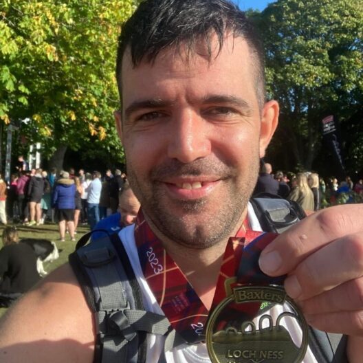CAP employee, Martin, at a Loch Ness Marathon finish line, holding up his medal and smiling
