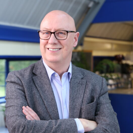 Stewart Mc Culloch, CEO of CAP UK, an older white man who is bald with glasses, wearing a suit, with crossed arms and smiling at the camera.