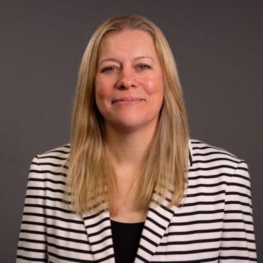 Headshot photo of CAP's Chief People Officer, Justine, wearing a black and white blazer, smiling at the camera