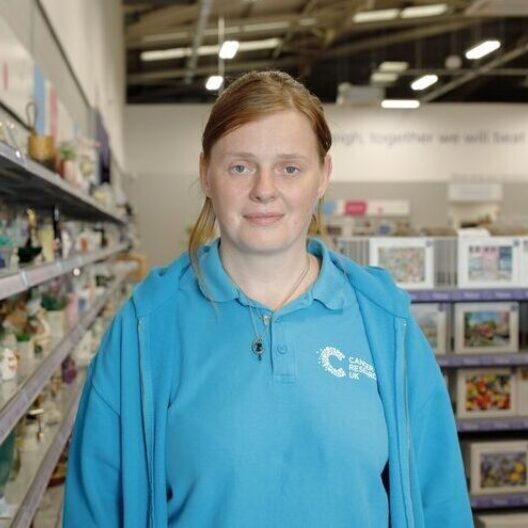 CAP client volunteering at her charity shop, smiling at the camera