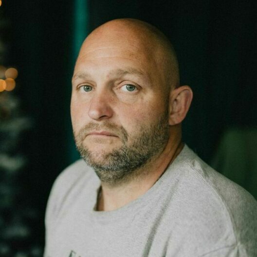 Man looking at the camera with sadness. There is a dark background around him