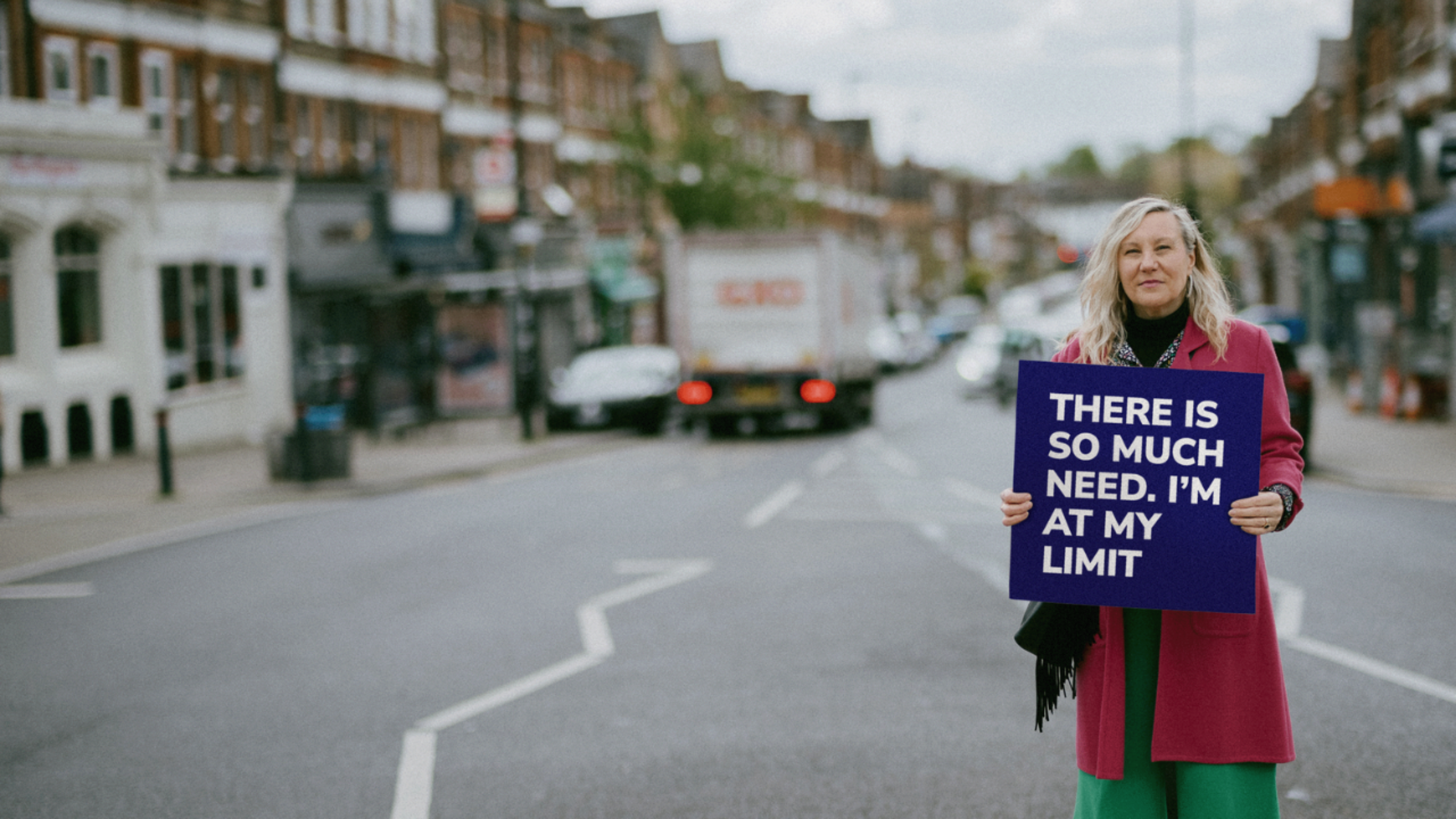 Ruth, co-Manager of her local CAP debt centre at Grace Church Brockley. She is standing on the street, wearing bold colours and holding a sign that reads 'There is so much need. I'm at my limit'
