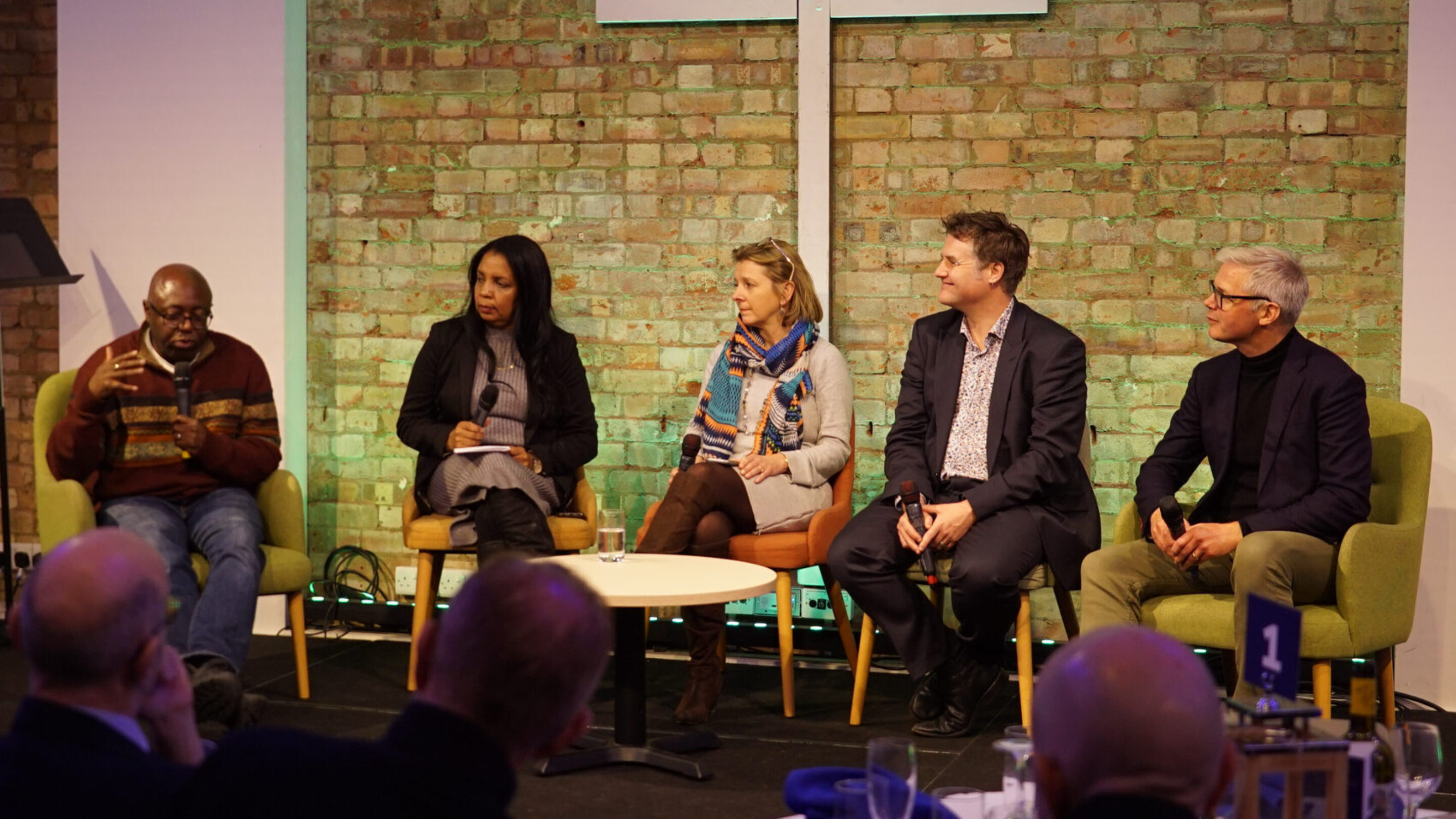 5 people sat on chairs on a stage, talking as part of a panel