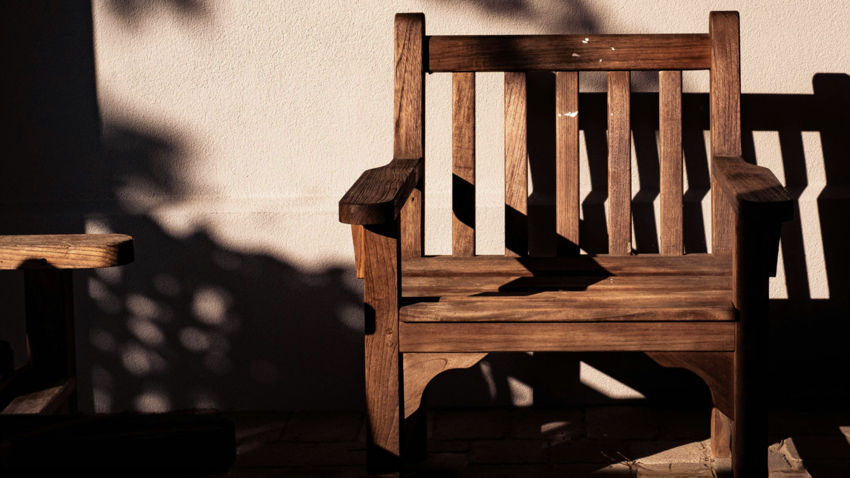 A photo of an outdoor wooden bench in the shadows of a garden