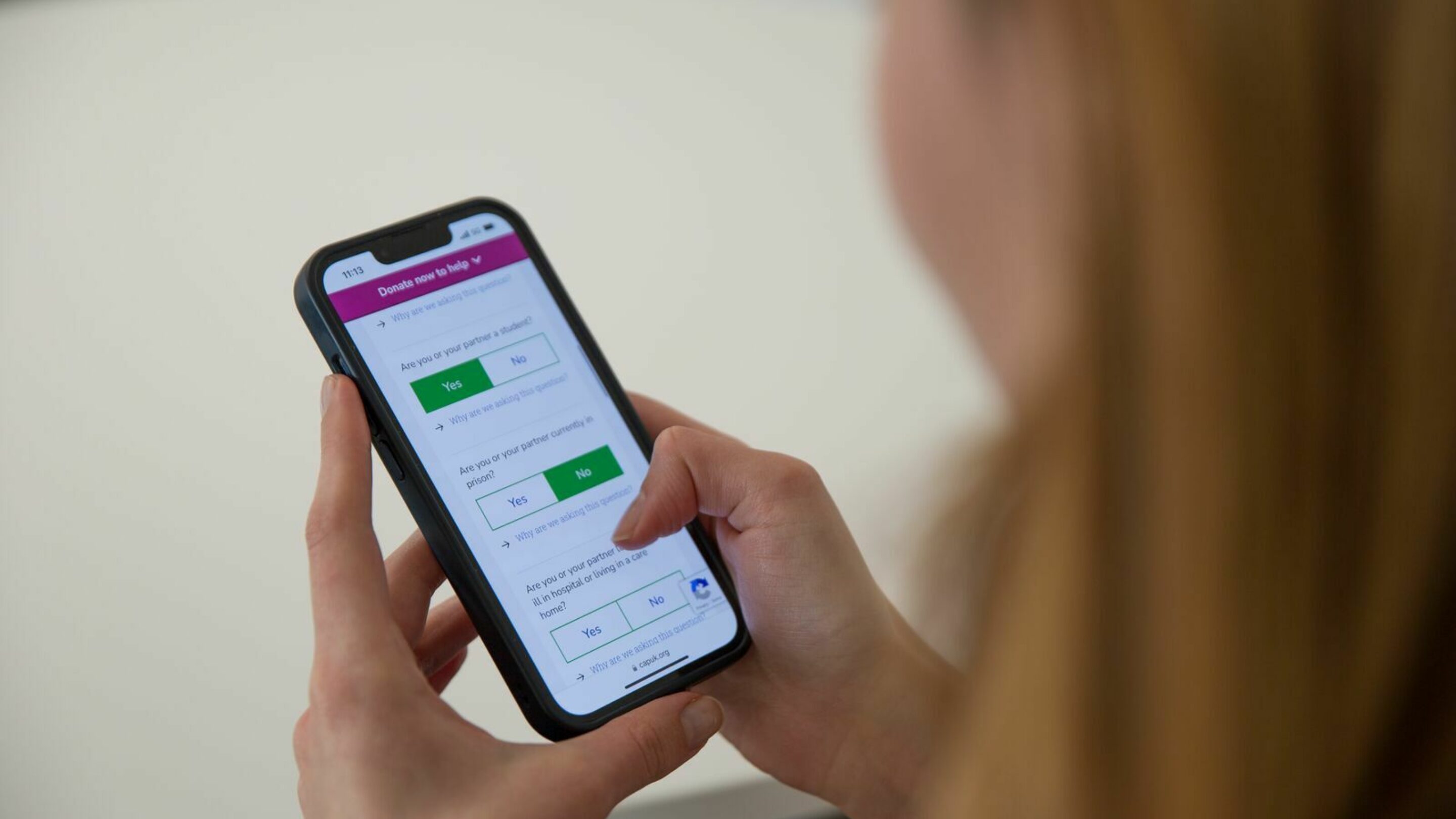 A person's hands holding a mobile phone, using CAP's benefits calculator (created in partnership with Turn2Us) to see what they're entitled to