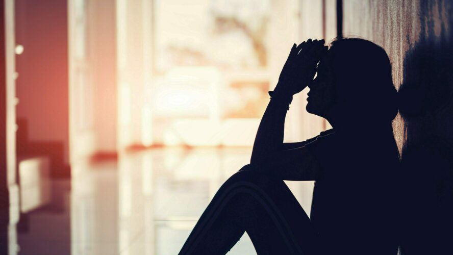 A dark silhouette of a woman sitting down with her head in her hands