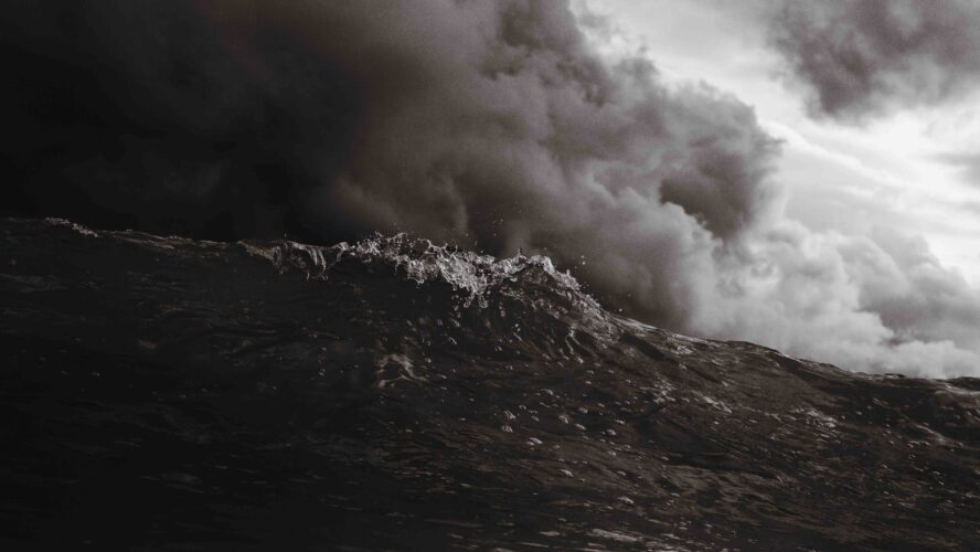 Black and white landscape image of dark clouds over crashing ocean waves