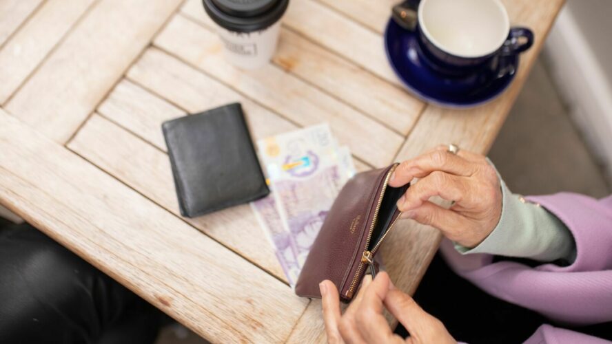 From above: a wooden table with coffee on it, and a purse. A lady is taking money out of her purse.