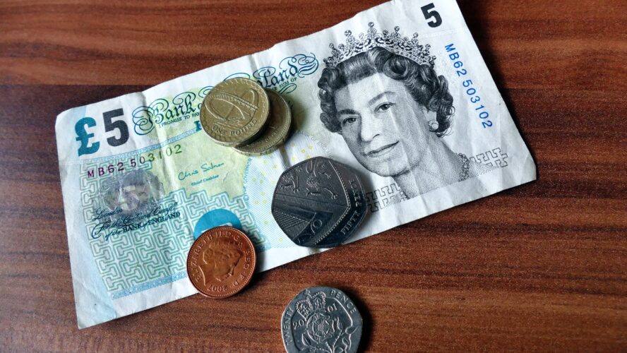 A five pound note, two pound coins, a 50p coin, 20p coin and 1p coin on a table, from above