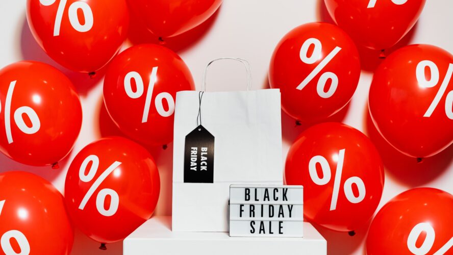 Several red balloons with percentage signs on, and a light box sign in the middle that reads Black Friday sale. Photo by Karolina Grabowska.