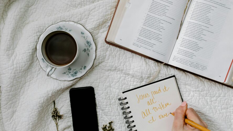 An open Bible, cup of tea, phone and notebook on a white blanket