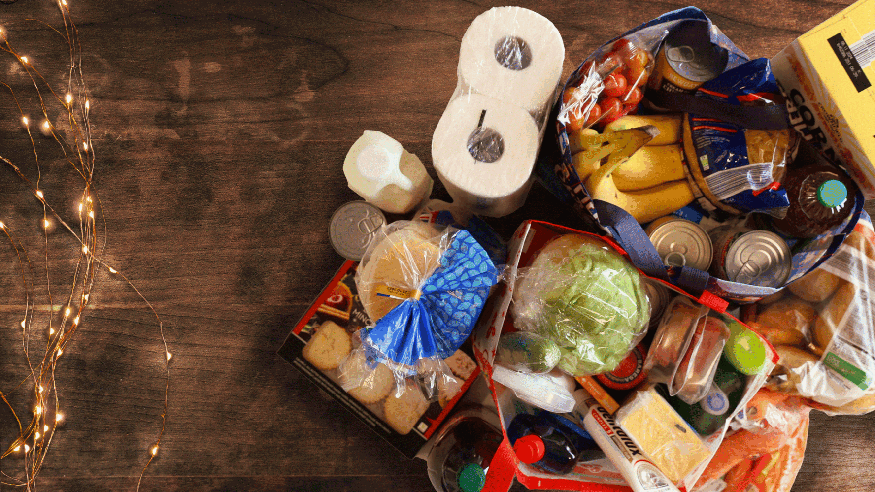 A Christmas hamper shown from above, filled with kitchen roll, bread, biscuits, bananas, cereal, salad, tins and more.