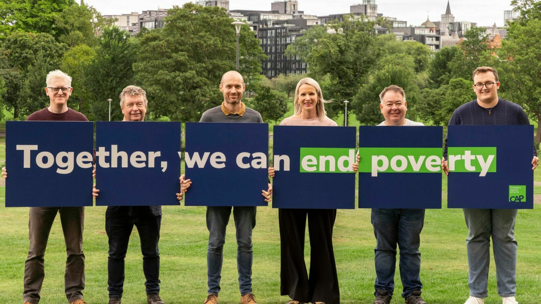Six people in a park holding navy blue signs that say 'together we can end poverty'