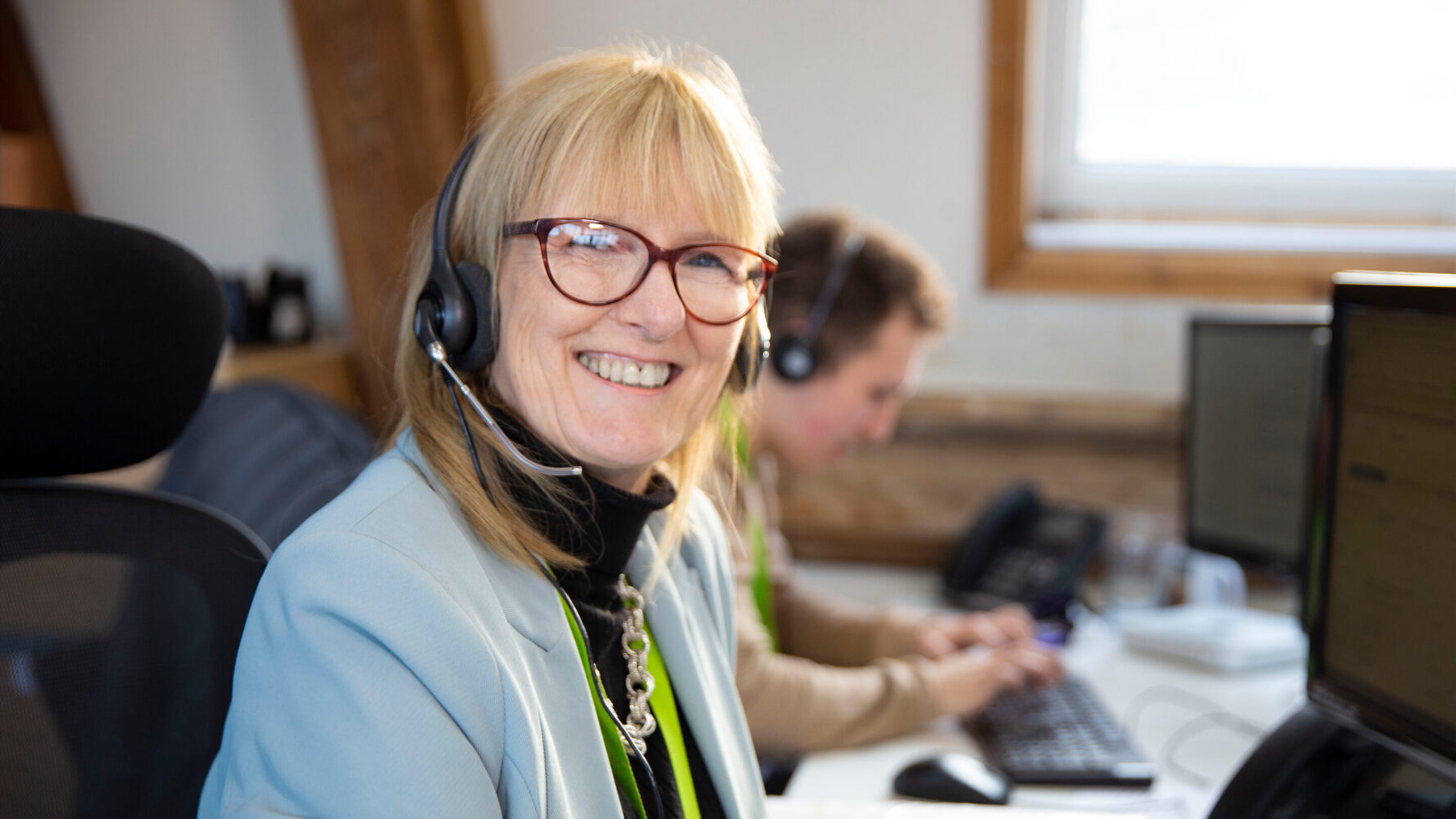 CAP employee, Sue, sat at her desk wearing a headset, smiling at the camera