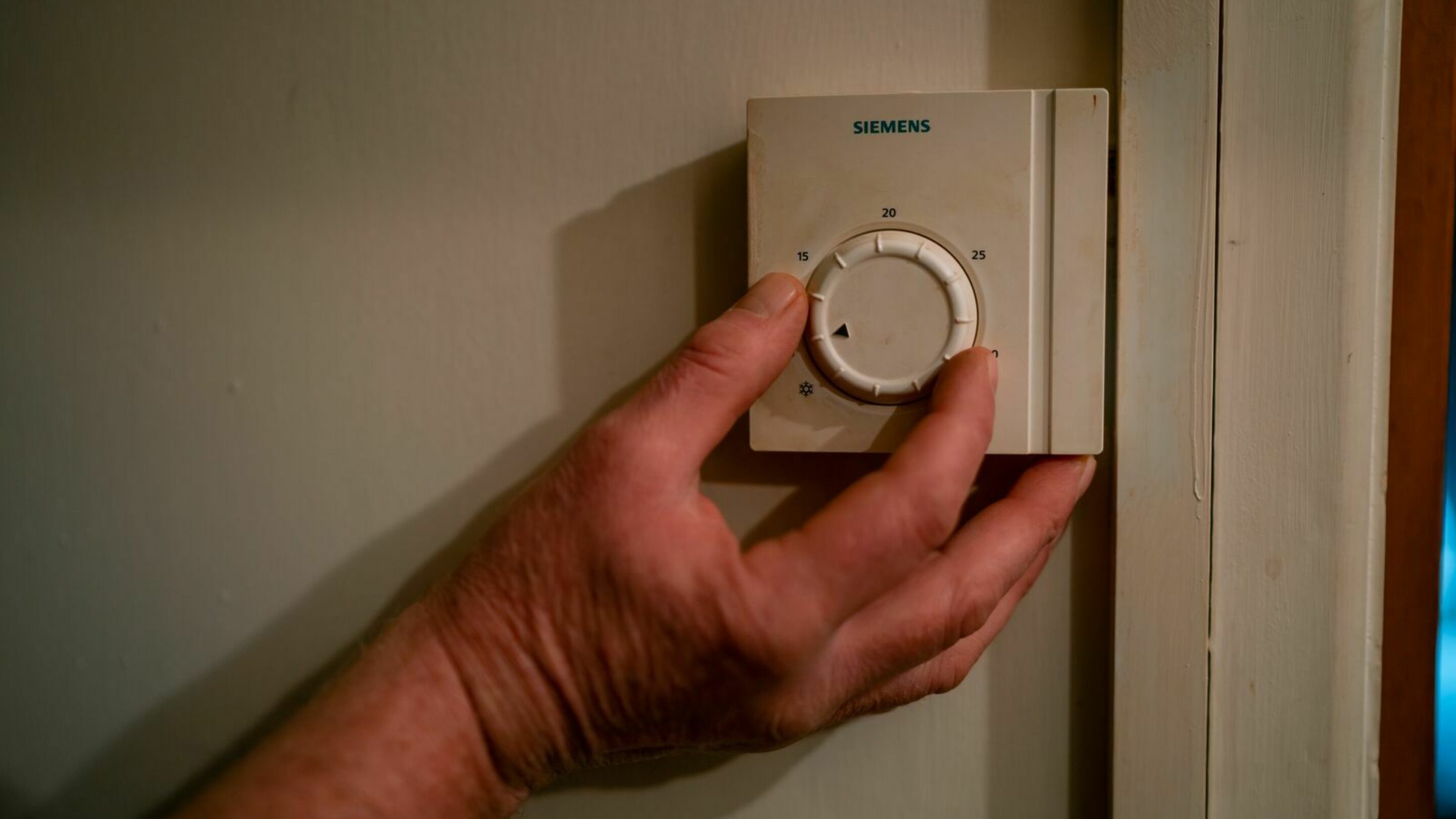 A man's hand adjusting the wall thermostat