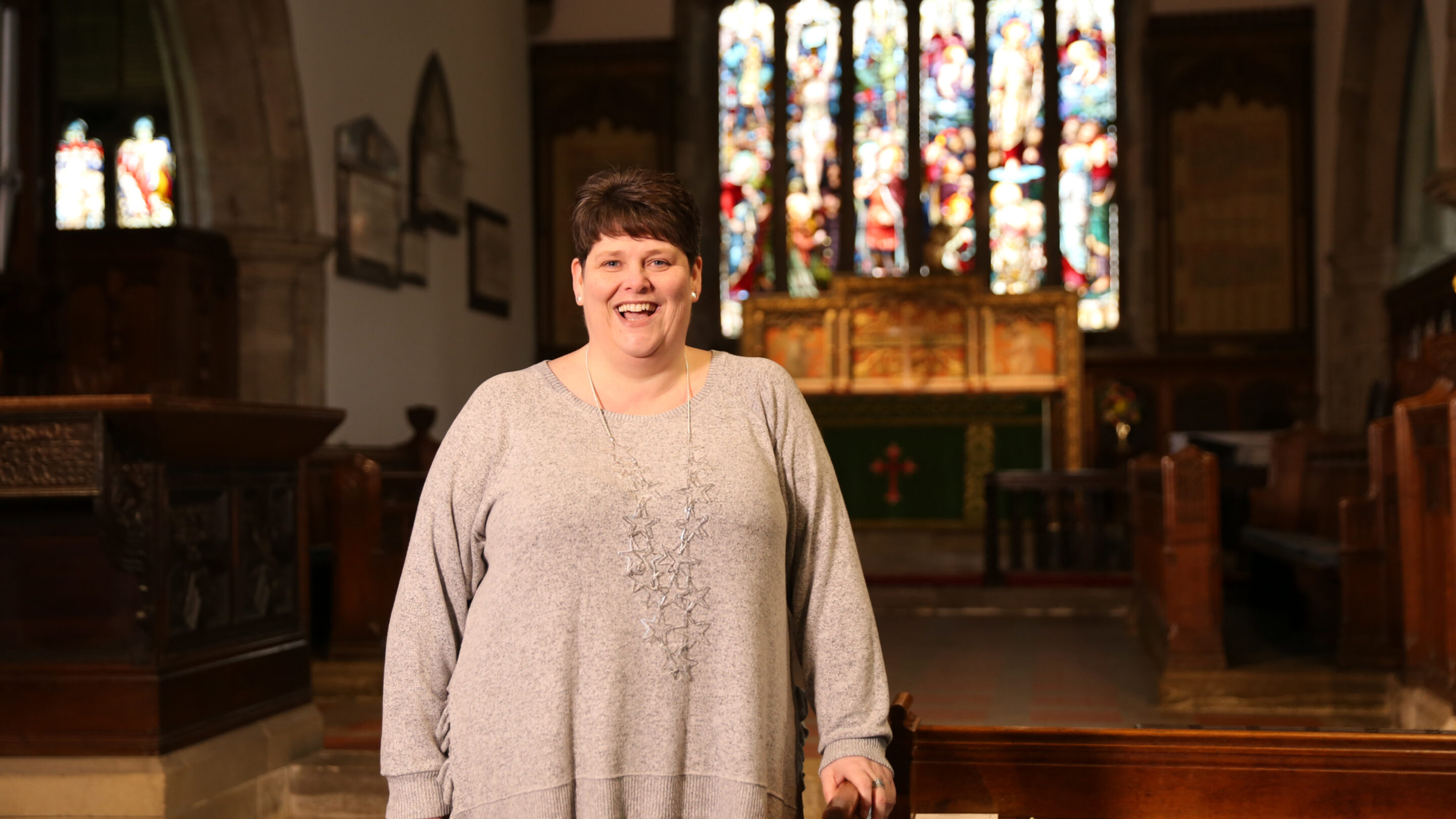 A cap client stood in their church. In the background there is an alter and a large stain-glass window.