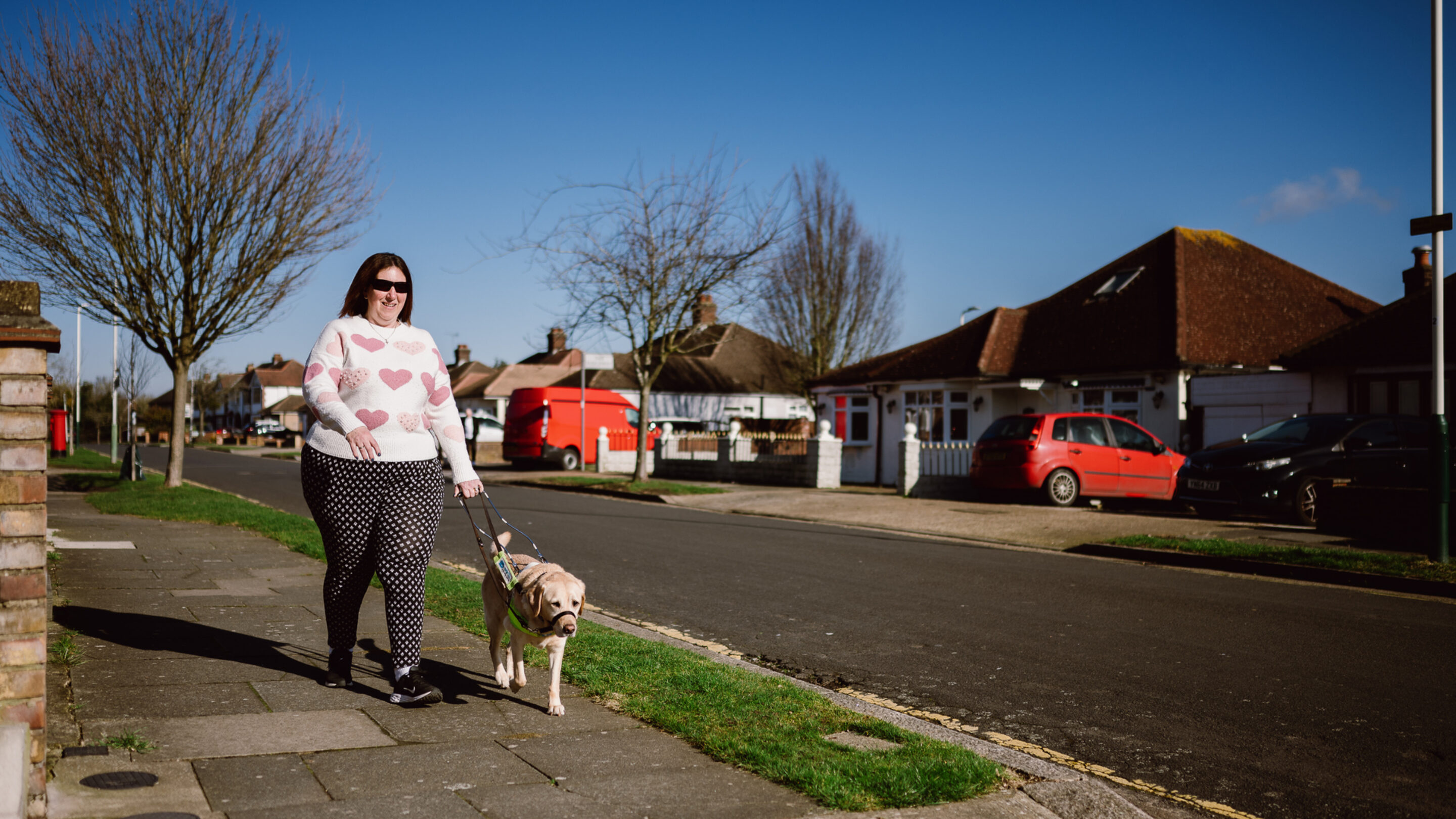 Angela, who lives with sight loss, and her guide dog, walking down the street