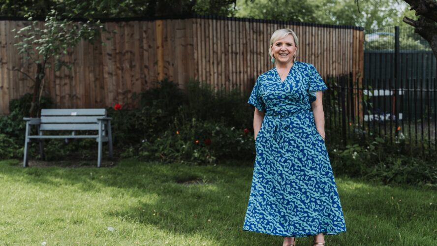 a woman in a blue dress smiles at the camera while standing in a garden