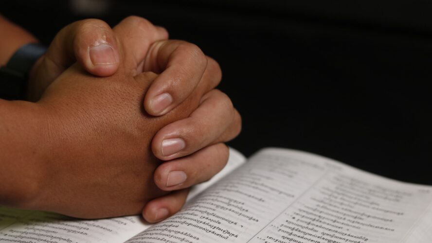 a pair of hands clasped in prayer resting on an open Bible