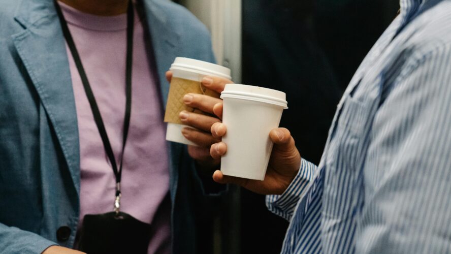 two people in business attire hold paper coffee cups