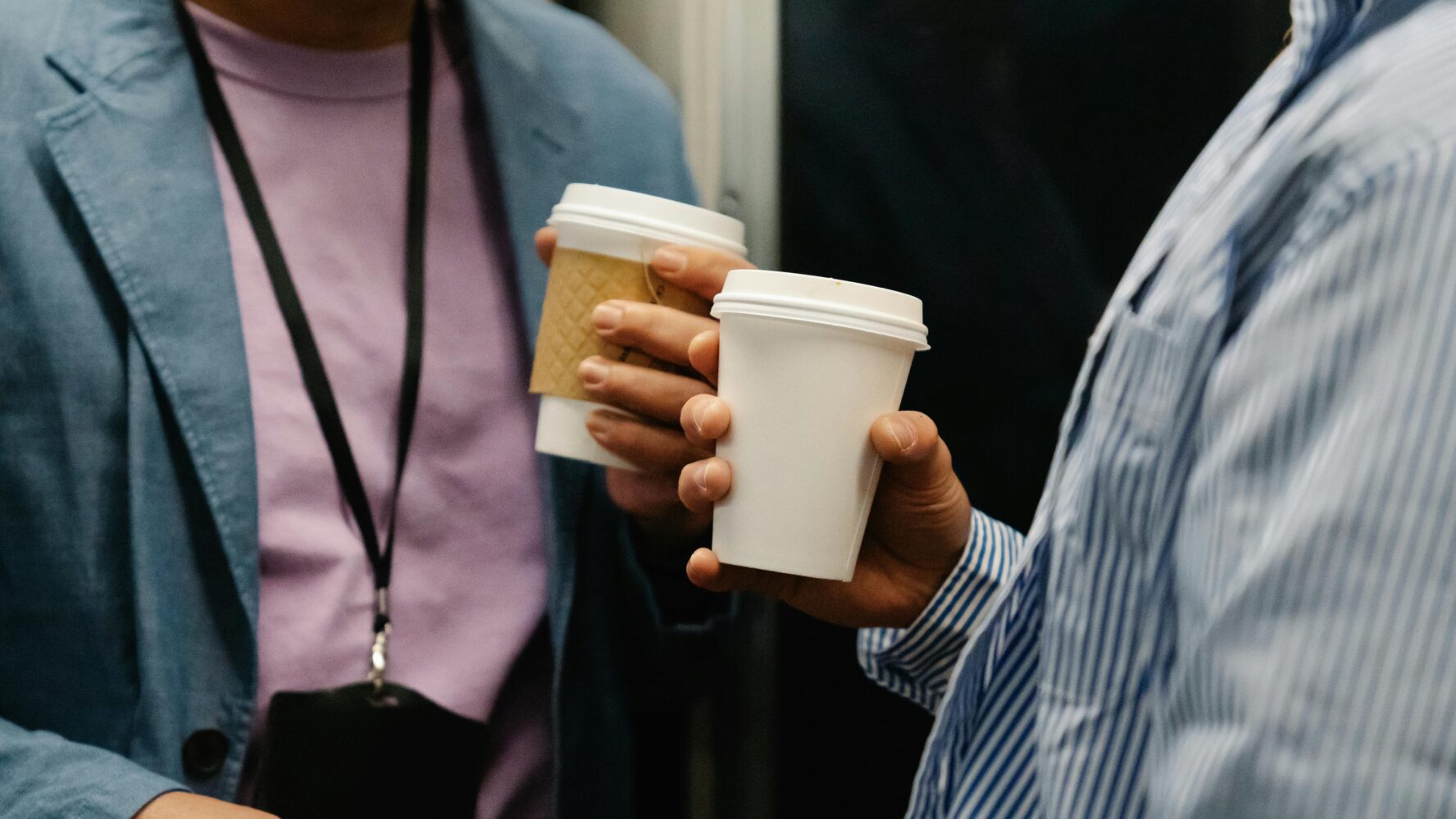 two people in business attire hold paper coffee cups