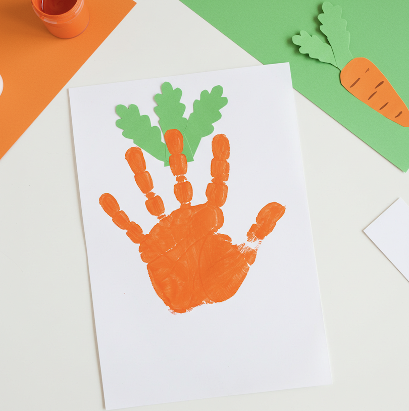 Image of an orange painted handprint on paper with green paint added to the top to look like a carrot