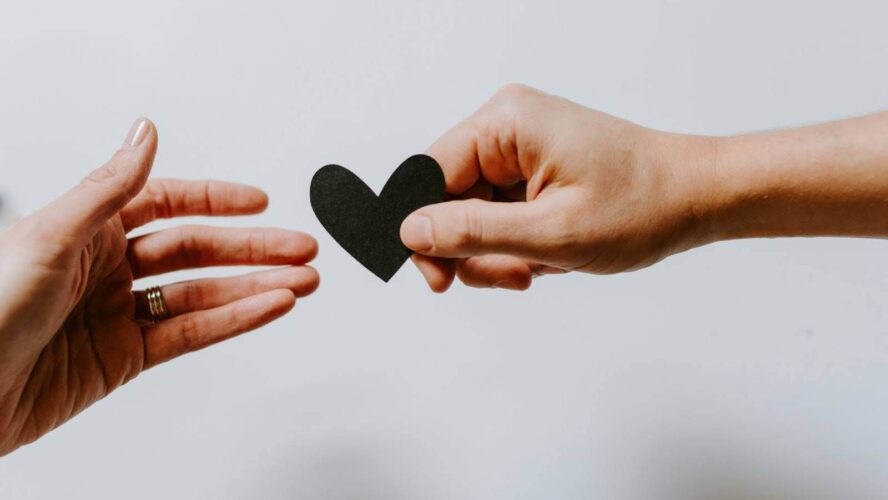 Image of two hands reaching towards each other, passing a piece of paper in the shape of a heart
