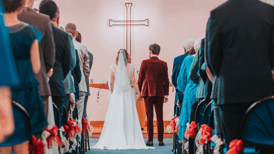 Taken from the wedding ceremony at a church, down the middle of the aisle. The happy couple are standing hand in hand facing the front, with their loved ones standing on either side. Photo by Matthew Leung (Tsz Lok Photos)..