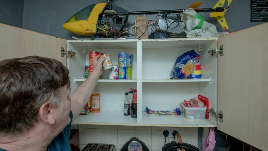 A man looks into an empty food cupboard in his kitchen