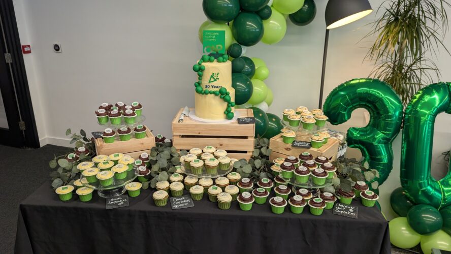 A table with a cake decorated with green balloons and the number 30, with a table full of cupcakes surrounding it and 30th green balloons.