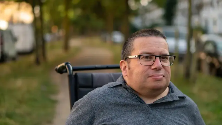 A man sat in a wheelchair outdoors in a park