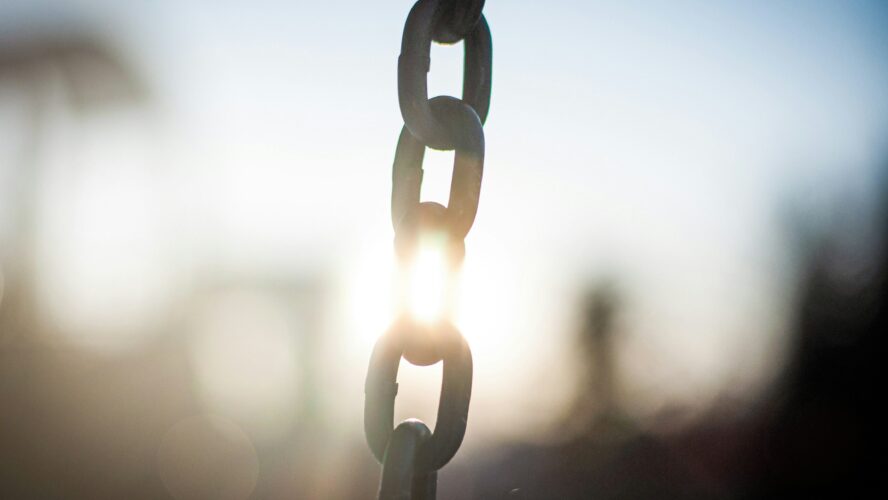 Image of a large metal chain in the middle of the photo, with the sun shining through behind it
