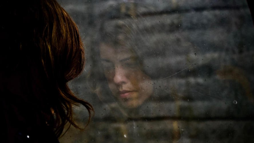 Person looking out of a window, their reflections showing a sad expression