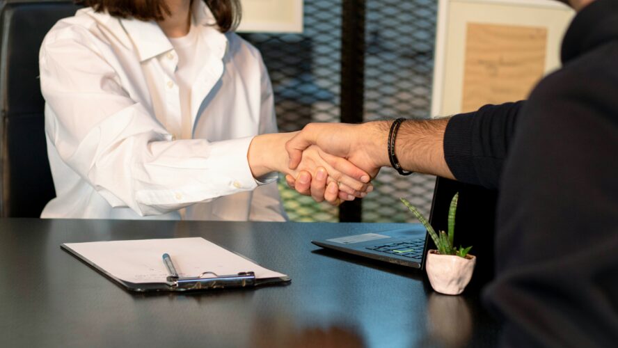 An interview showing a woman and a man shaking hands across a table