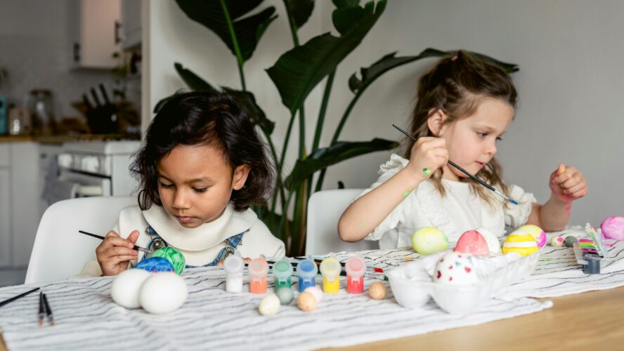 Two children sat at a table, painting eggs with colourful paints