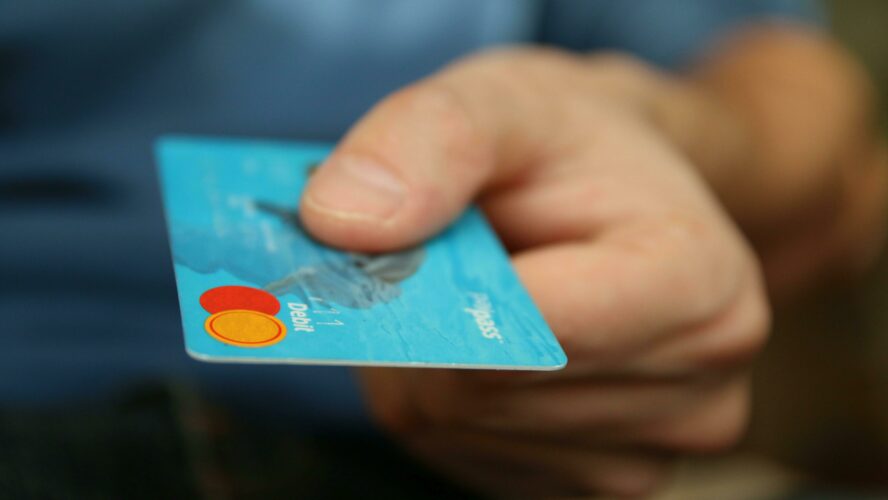 a hand holds out a debit card, as if about to pay for a transaction