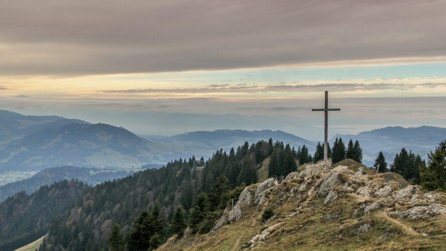 Image of a green hill landscape with a wooden cross on the top of the hill
