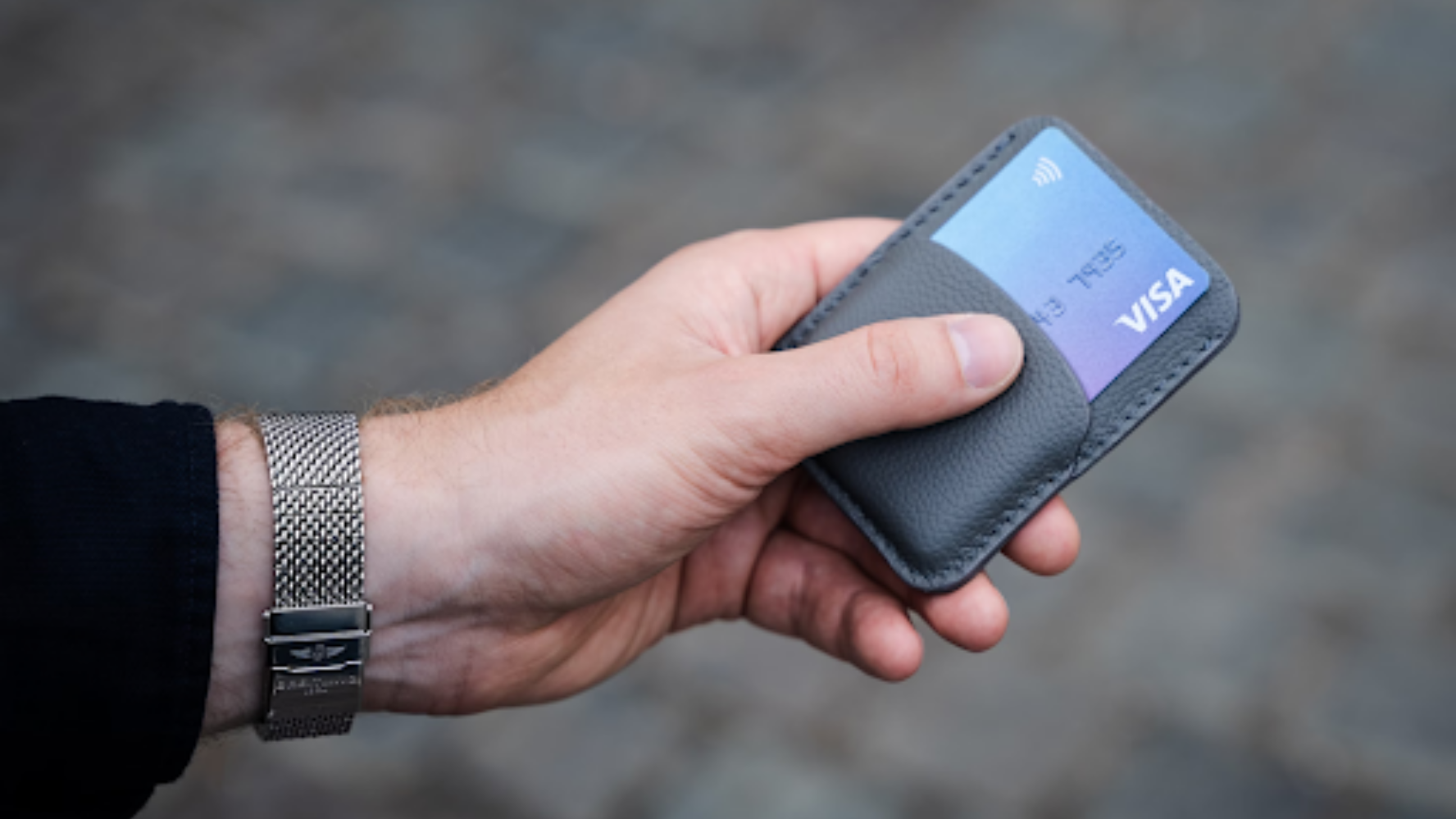 Image of a person's left hand, holding a wallet with a credit card in it