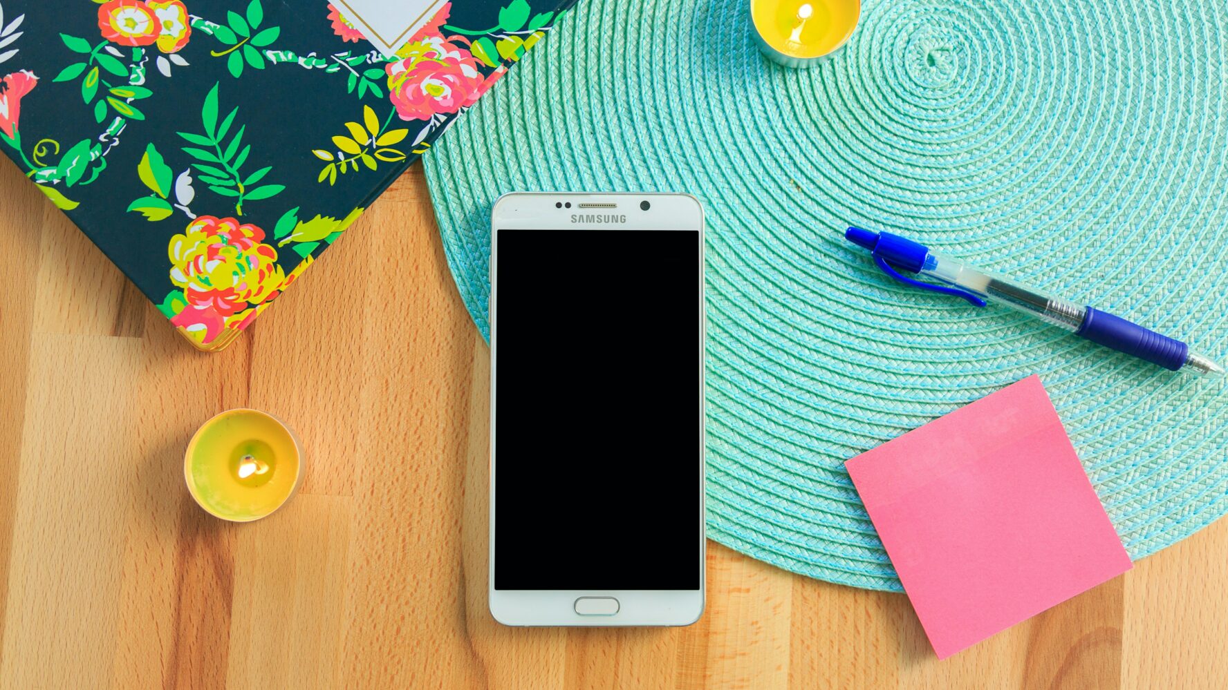 A phone on a desk next to a notebook, pen, and tealights