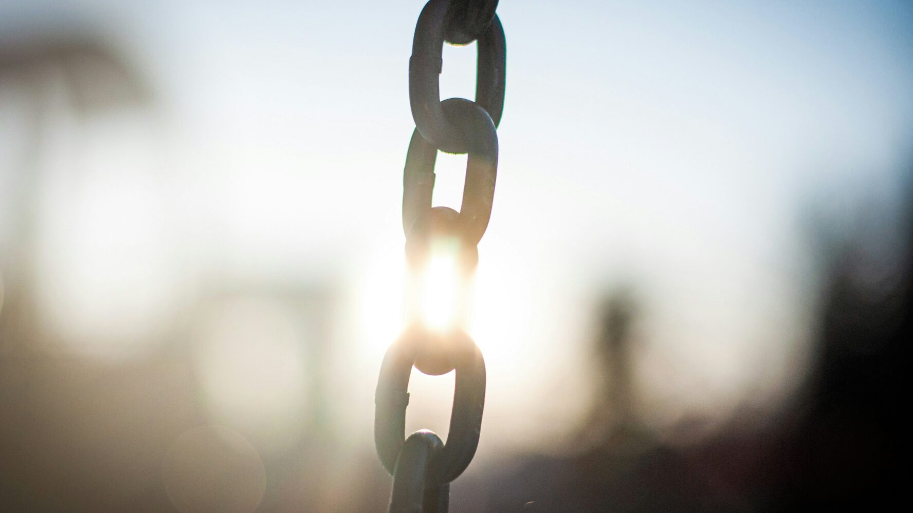 Image of a large metal chain in the middle of the photo, with the sun shining through behind it
