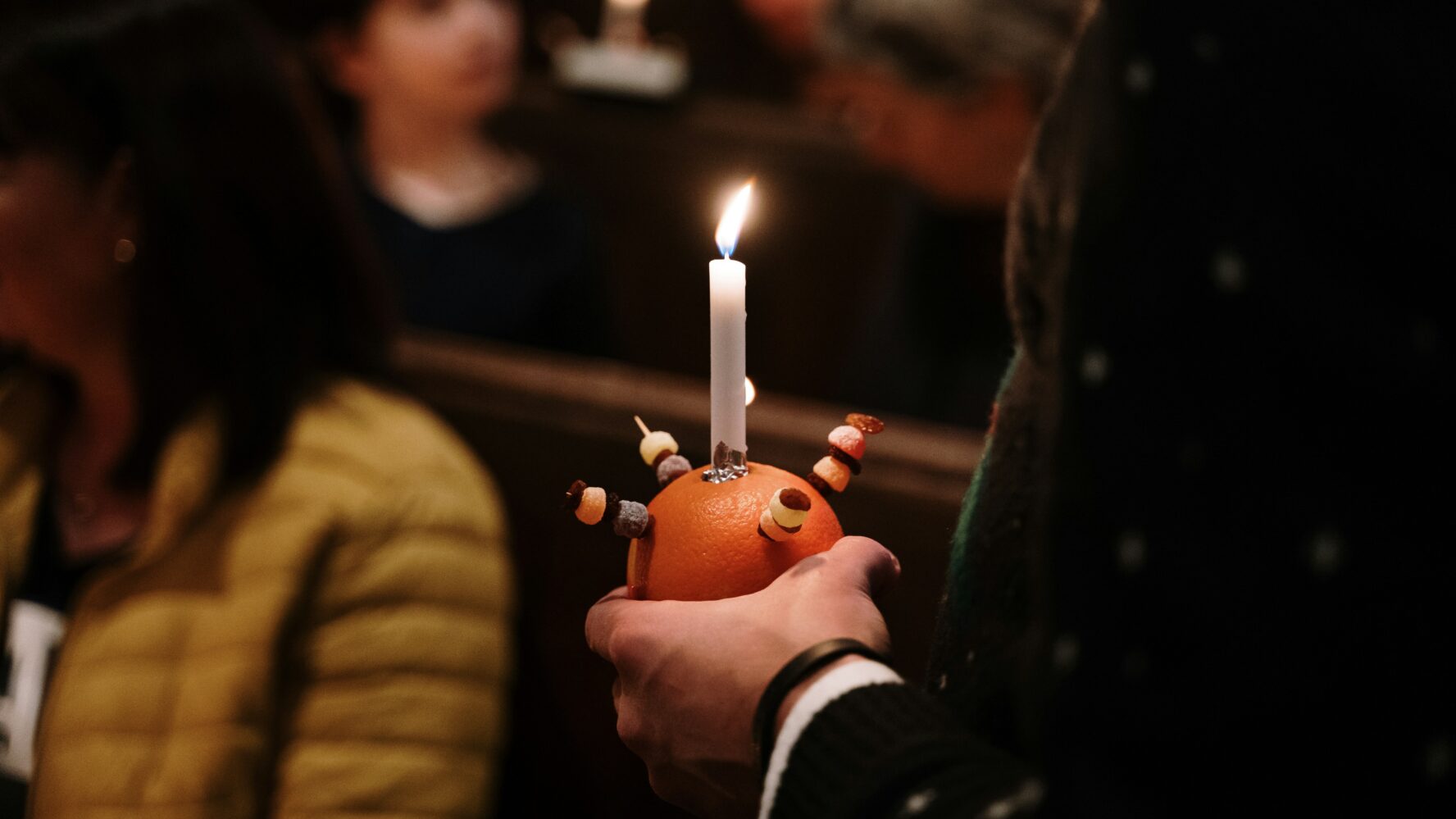 Someone at a Christingle church service, holding an orange with a candle in it