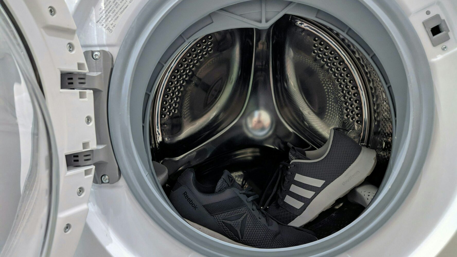 Picture of a washing machine with the door open and two pairs of trainers inside