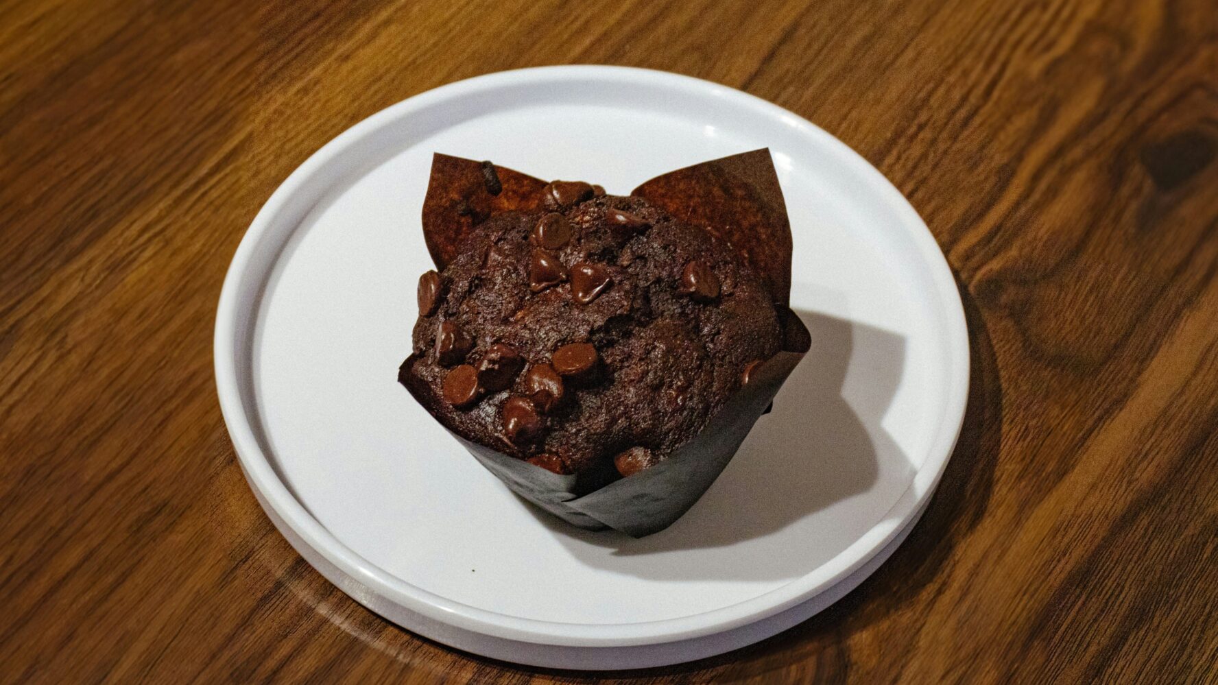 A chocolate muffin on a white plate on a wooden table
