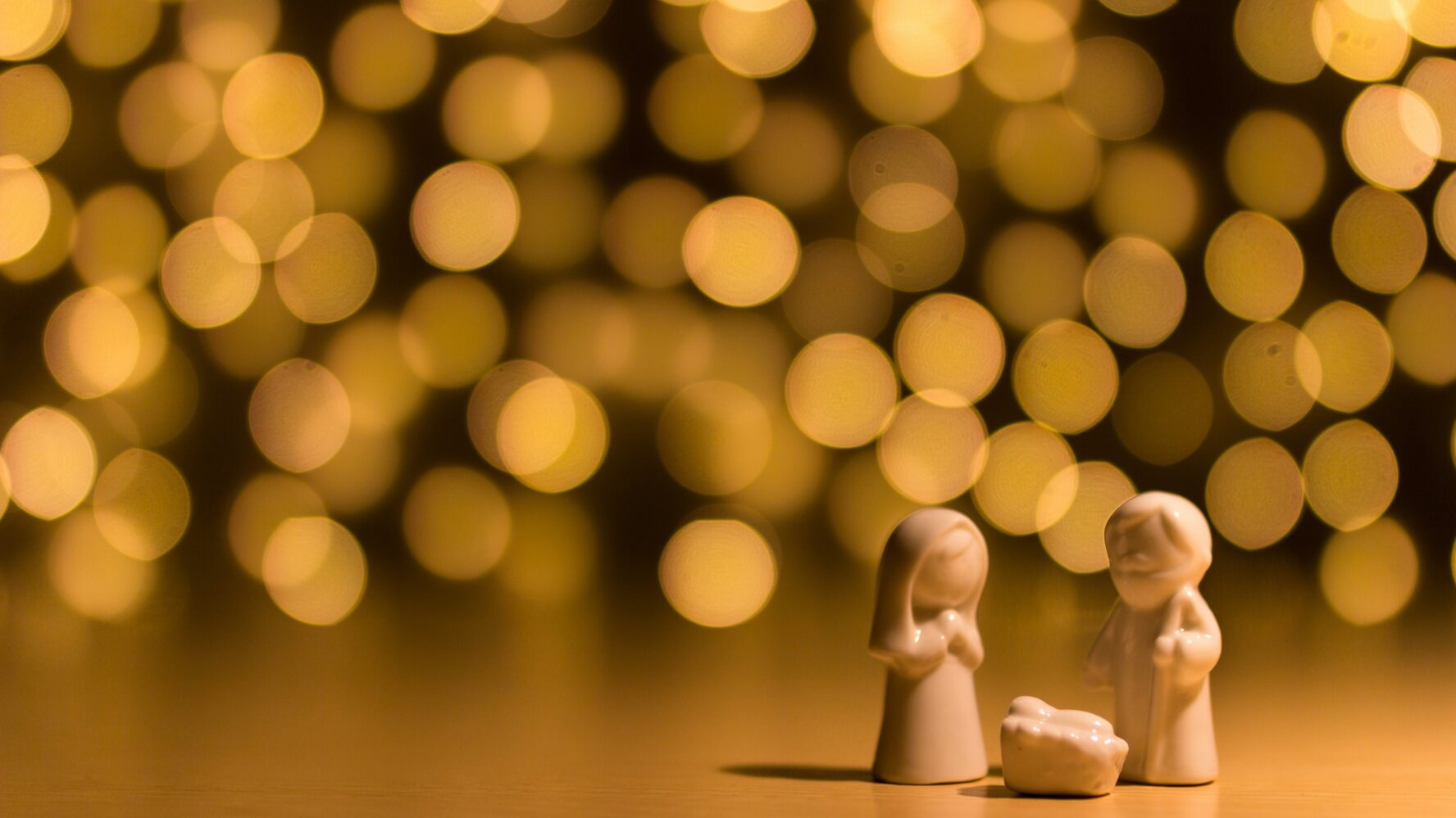 A amll nativity scene made out of white marble, with fairy lights in the background