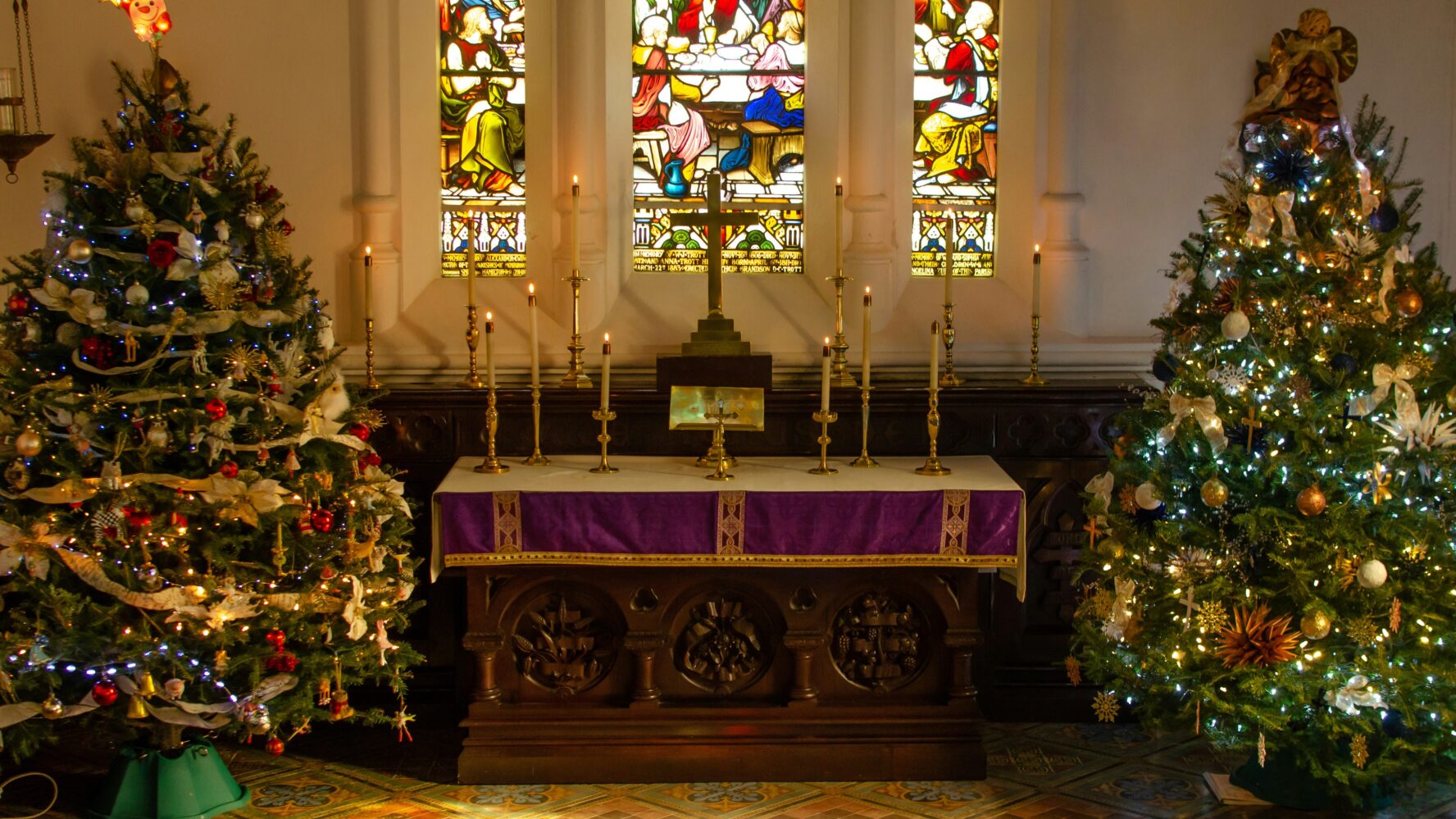 A Church table with pillar candles on it, with two large Christmas trees either side.