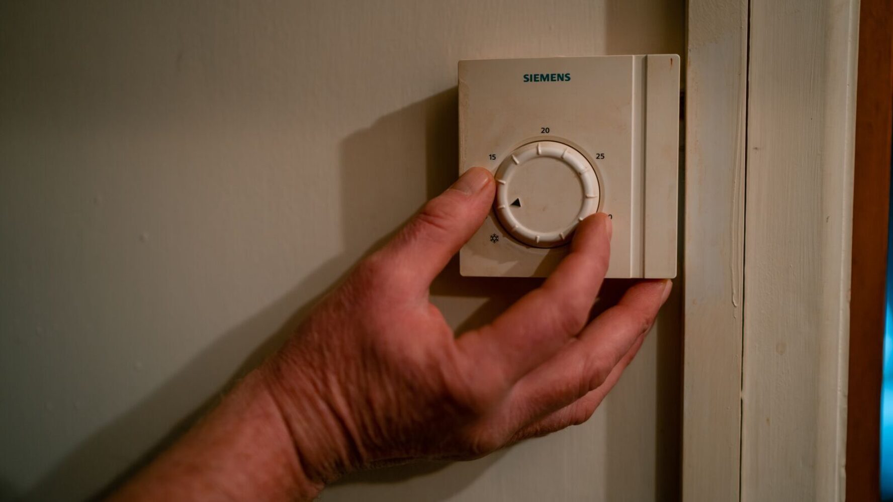 Person's hand turning down their thermostat in their home