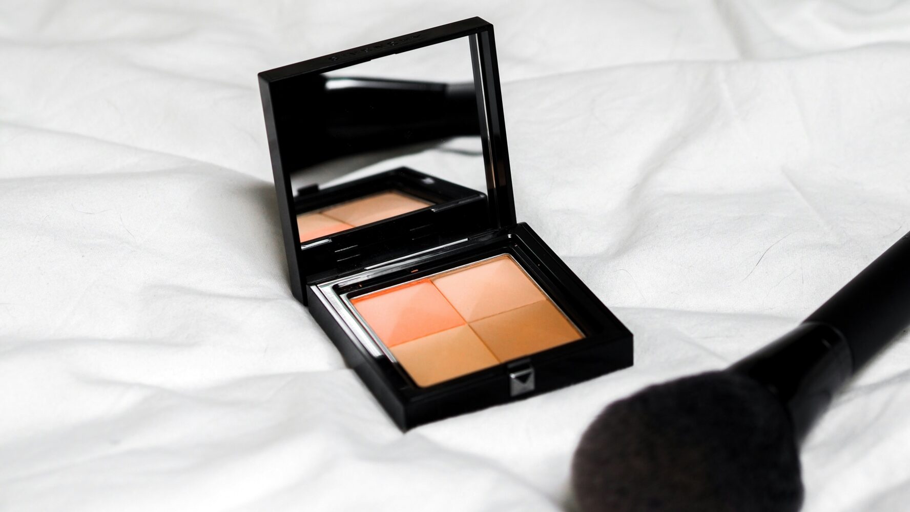 A cosmetic blush palette with a mirror, and a black blush brush next to it